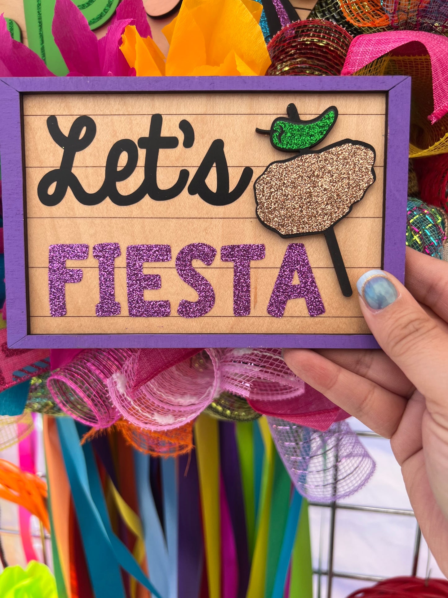 Decorative sign with 'Let's Fiesta' text with chicken on a stick graphic against a colorful background.