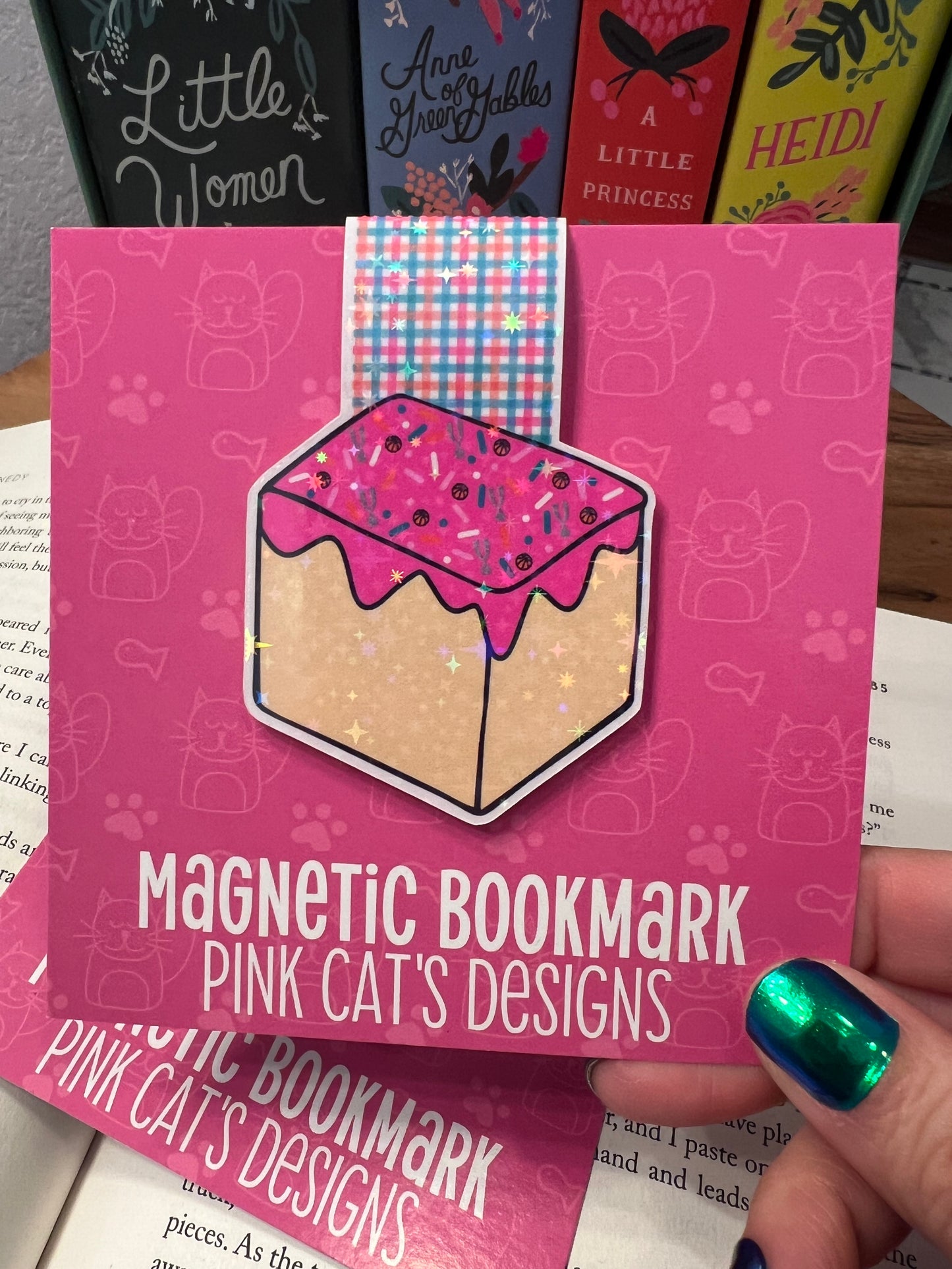 Pink magnetic bookmark packaging with a sample bookmark on top, held by a hand.