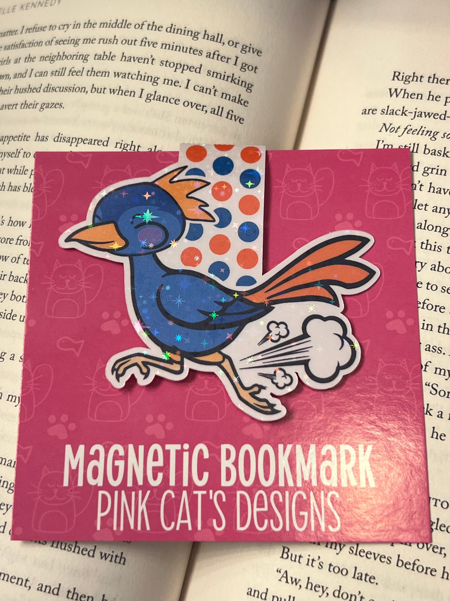 Magnetic bookmark with cartoon roadrunner design on a pink background, placed on a book page.