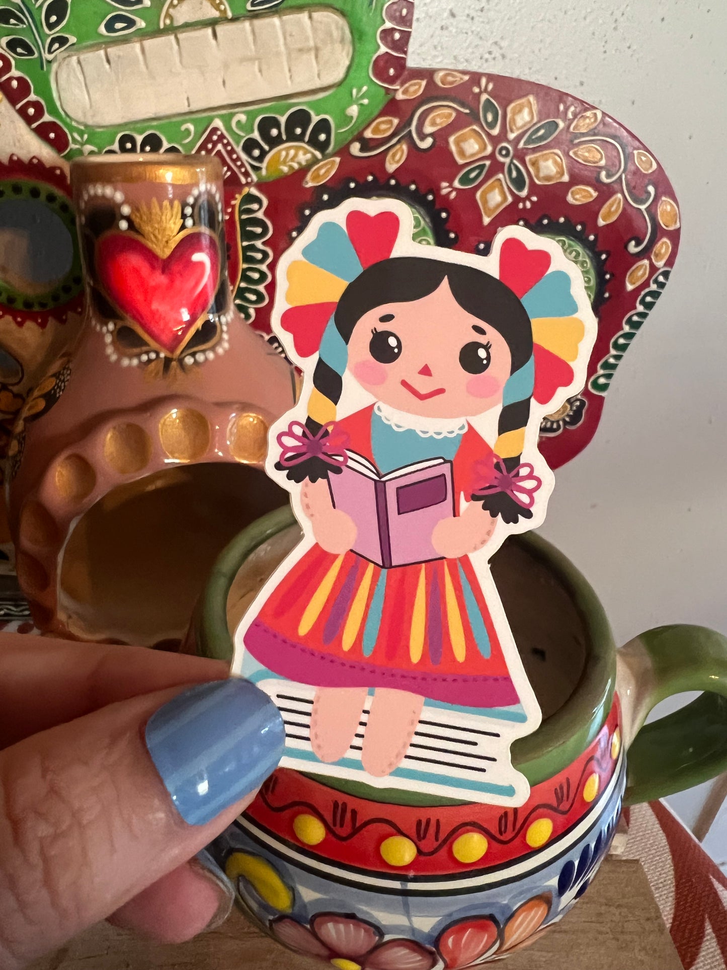 colorful designs and a hand holding a sticker of a doll with a book.