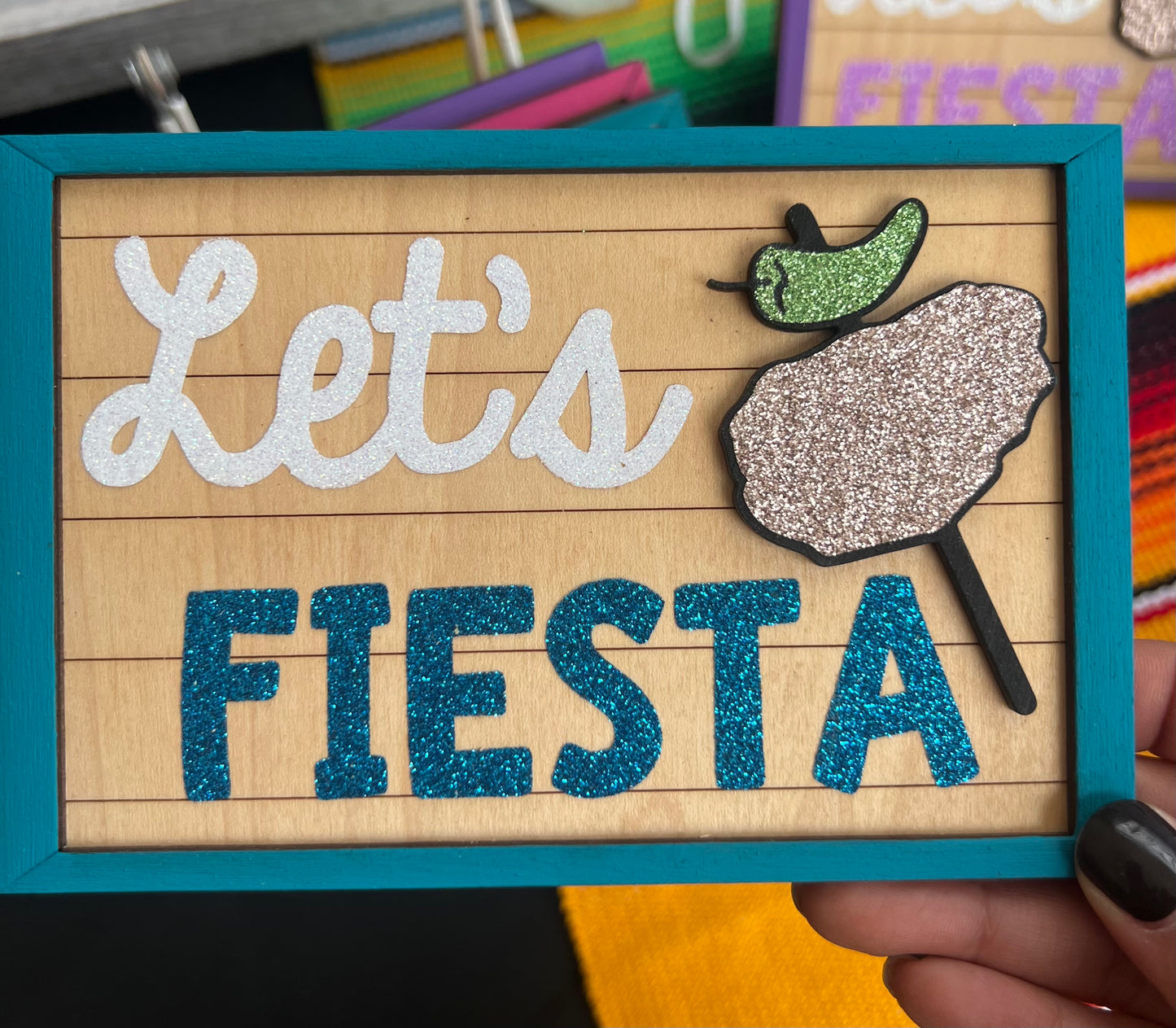 Decorative sign with 'Let's Fiesta' text and decorative chicken on a stick  held by a hand.