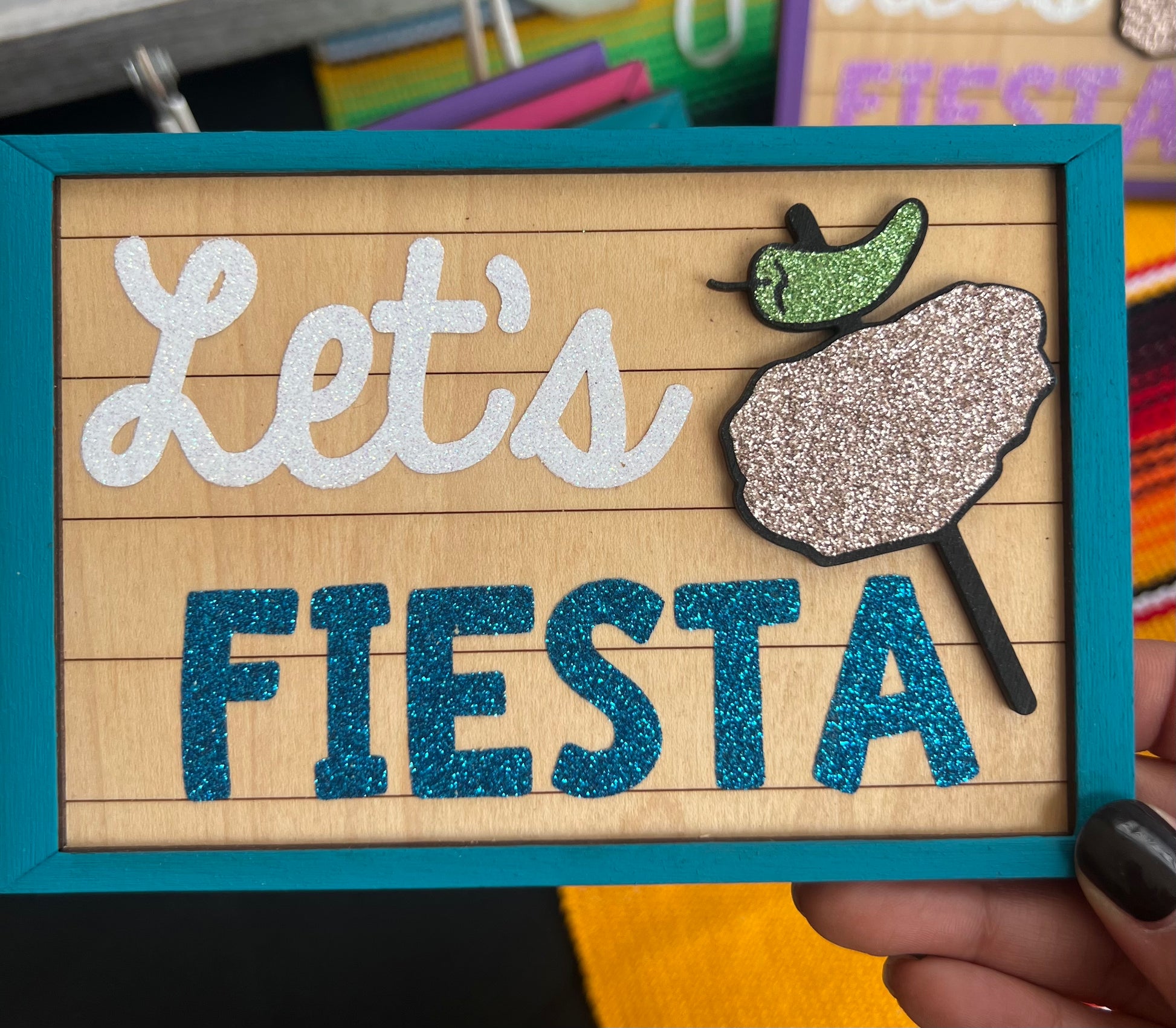 Decorative sign with 'Let's Fiesta' text and decorative chicken on a stick  held by a hand.