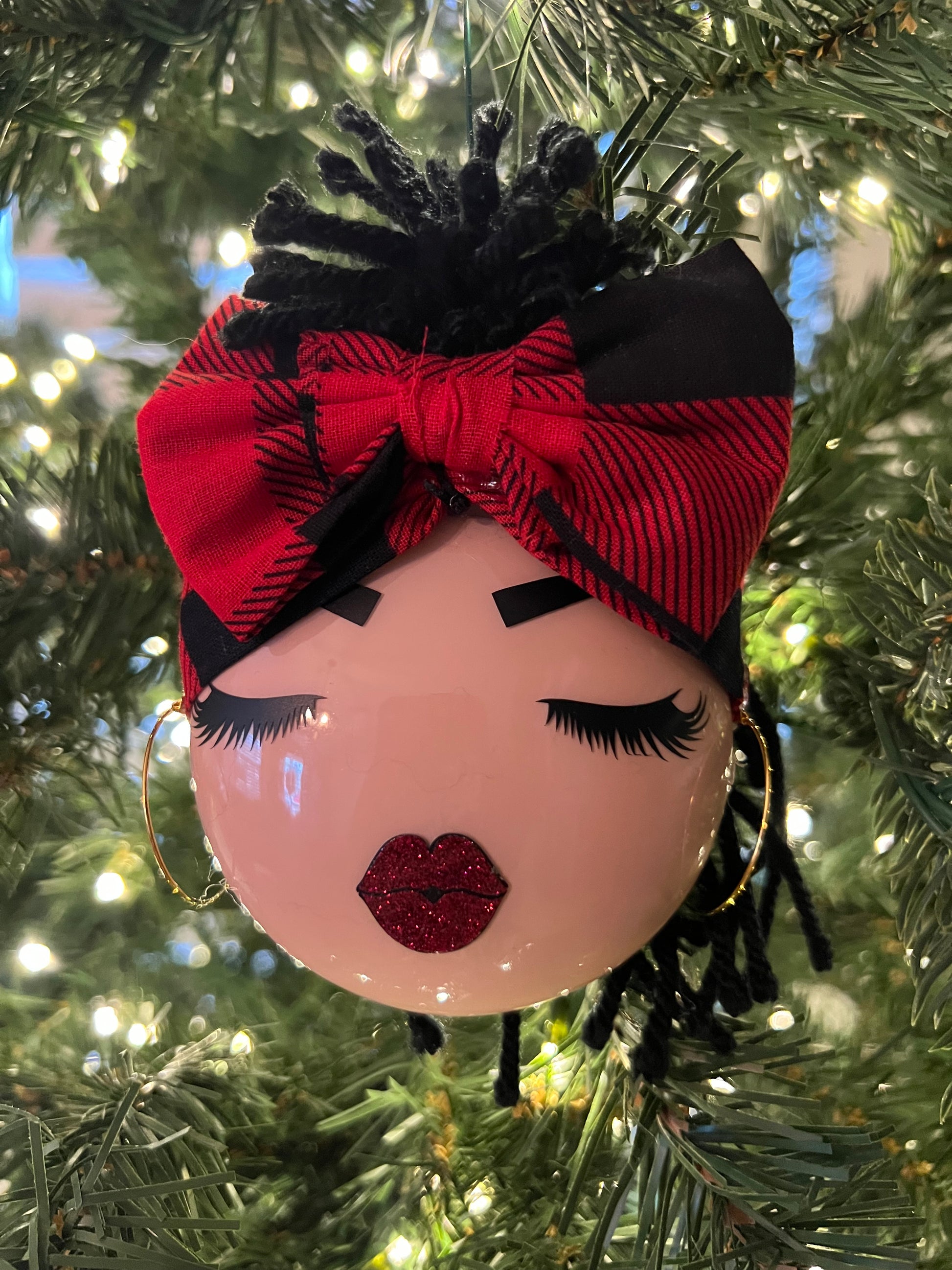 Decorative ornament shaped with woman’s face with a red and black bandana on a Christmas tree.