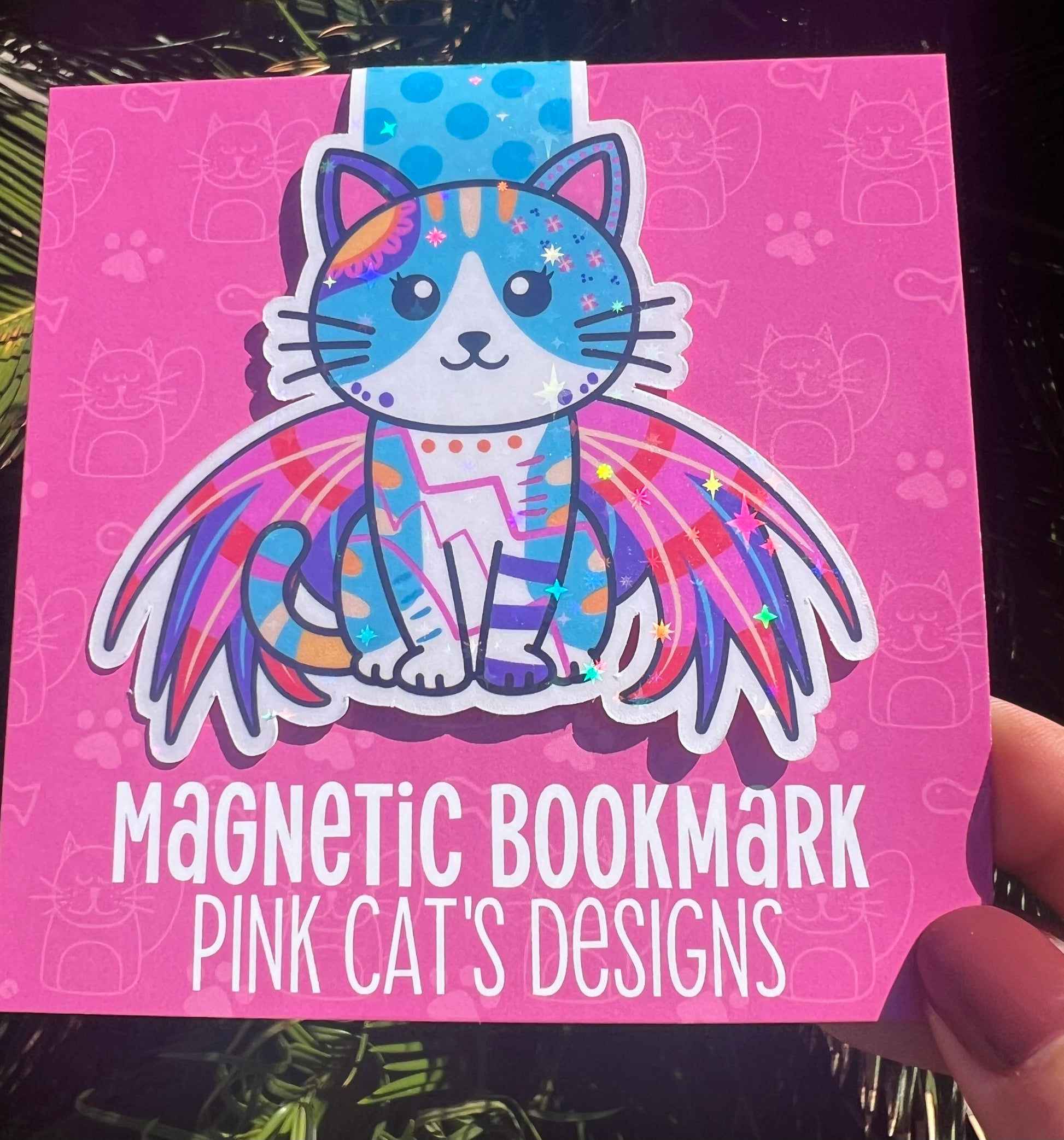 Magnetic bookmark with a colorful cat design on a pink background, held by a hand.