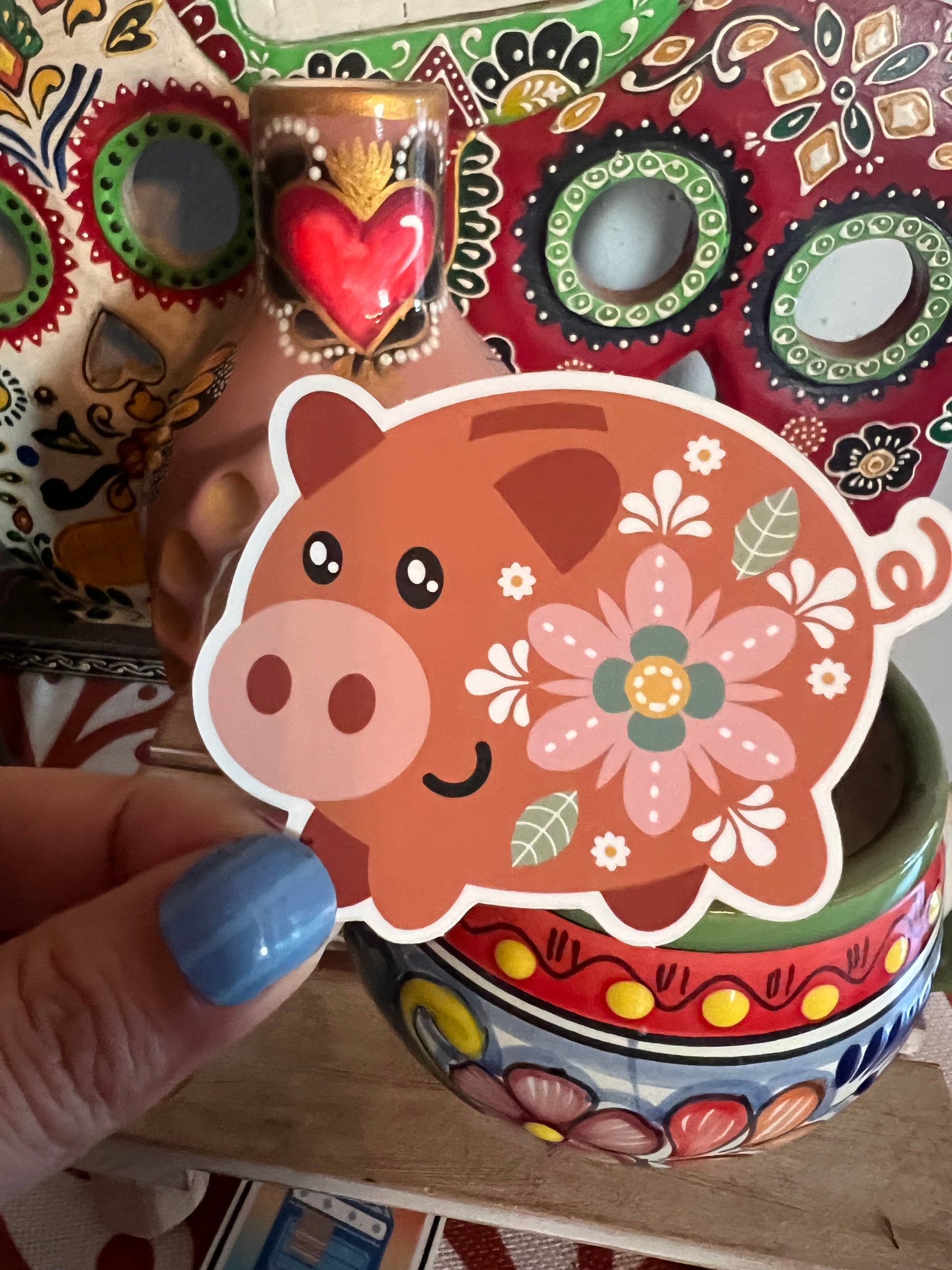 Decorative sticker with a floral pig design held by a hand with blue nail polish.
