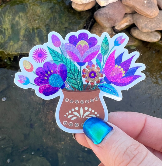 Colorful flower vase sticker held by a hand with blue nail polish against a natural background.