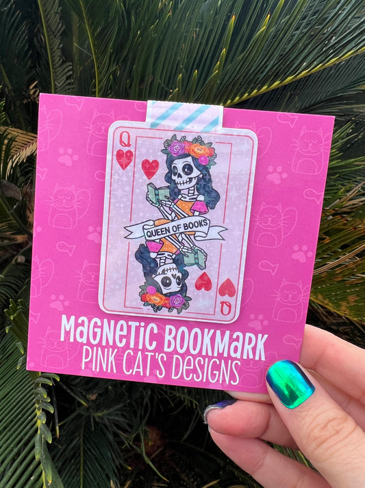 Pink magnetic bookmark with a colorful design held by a hand against a green leafy background