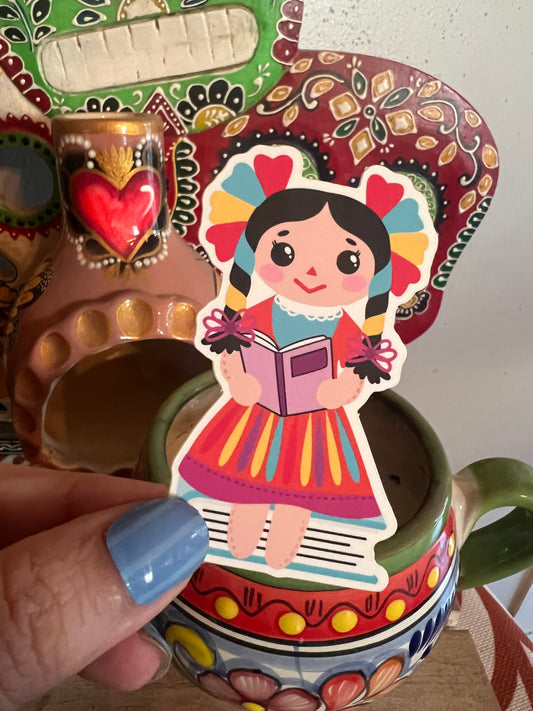 colorful designs and a hand holding a sticker of a doll with a book.