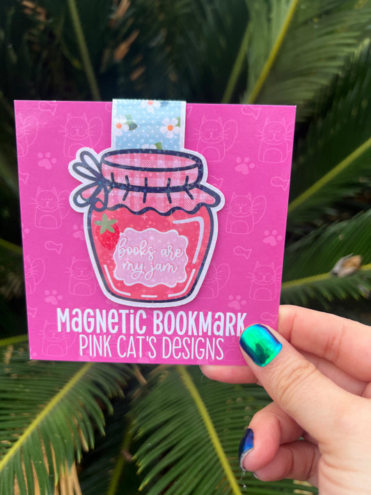 Pink magnetic bookmark with a design held by a hand against a green leafy background